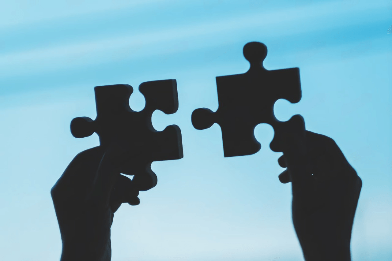 Hands holding puzzle pieces against sky
