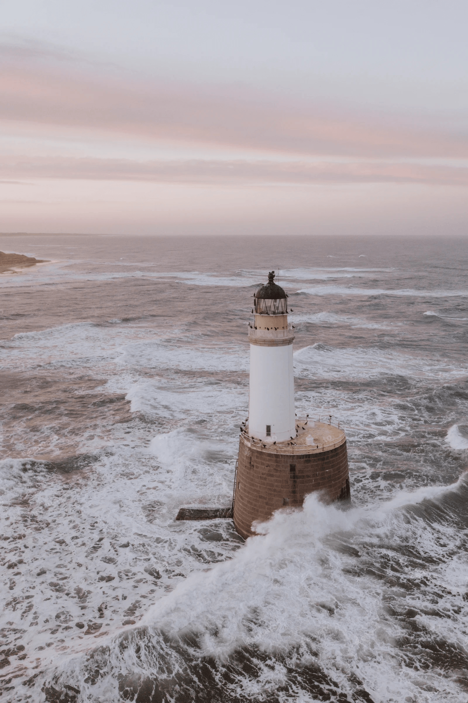 Lighthouse amidst ocean waves during sunset