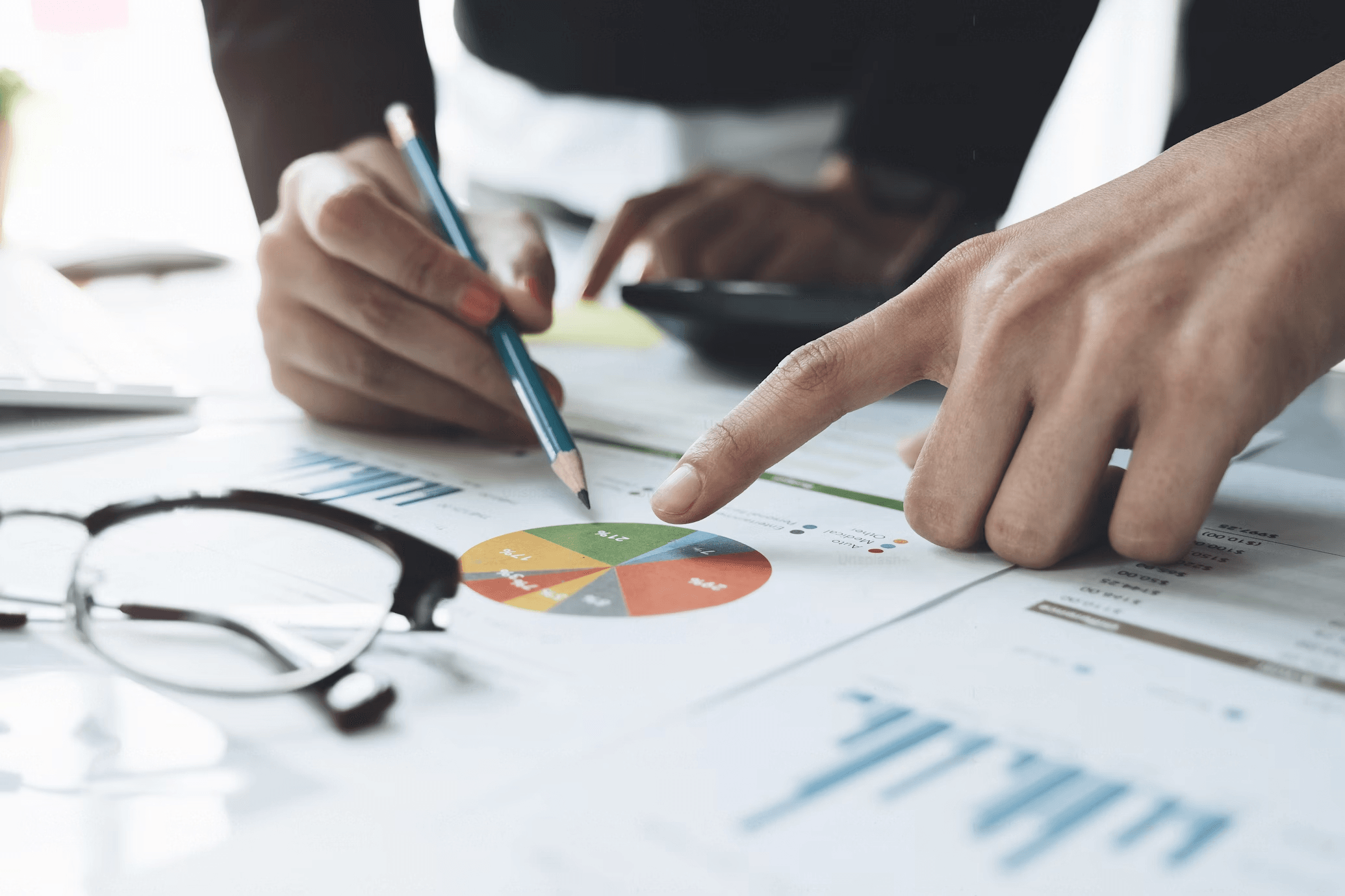 Hands analyzing colorful pie chart on paper.